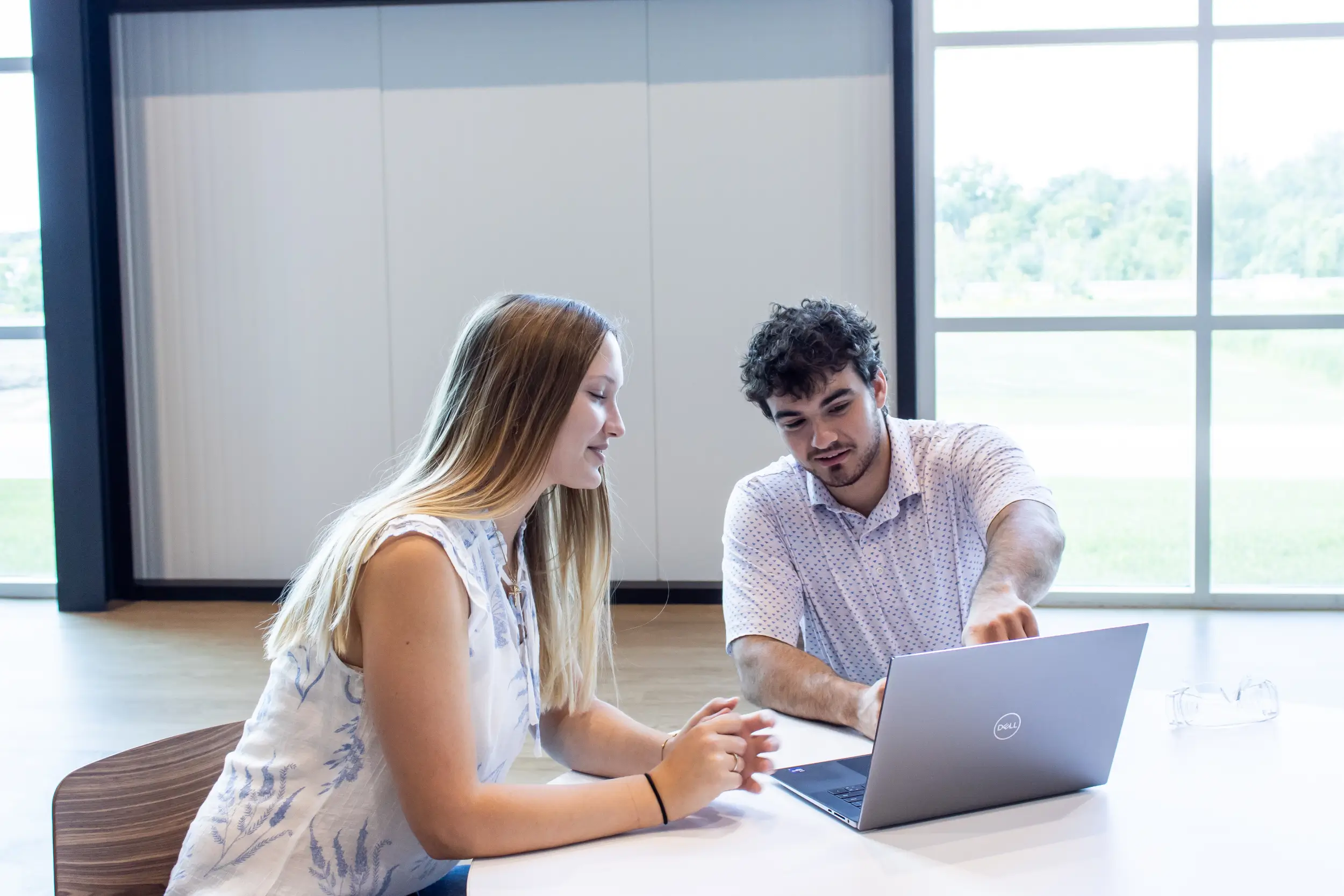 A man and a woman are working on laptops and discussing.